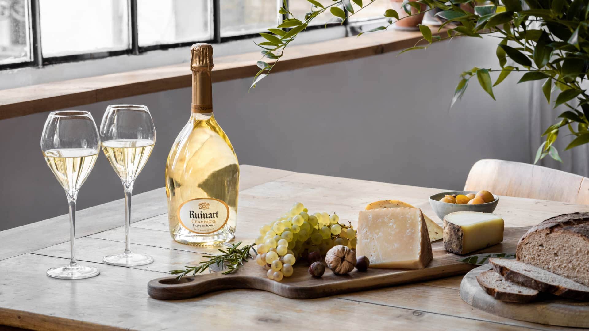 Ruinart Blanc de Blancs champagne, glas, druer, ost og brød på et træbord
