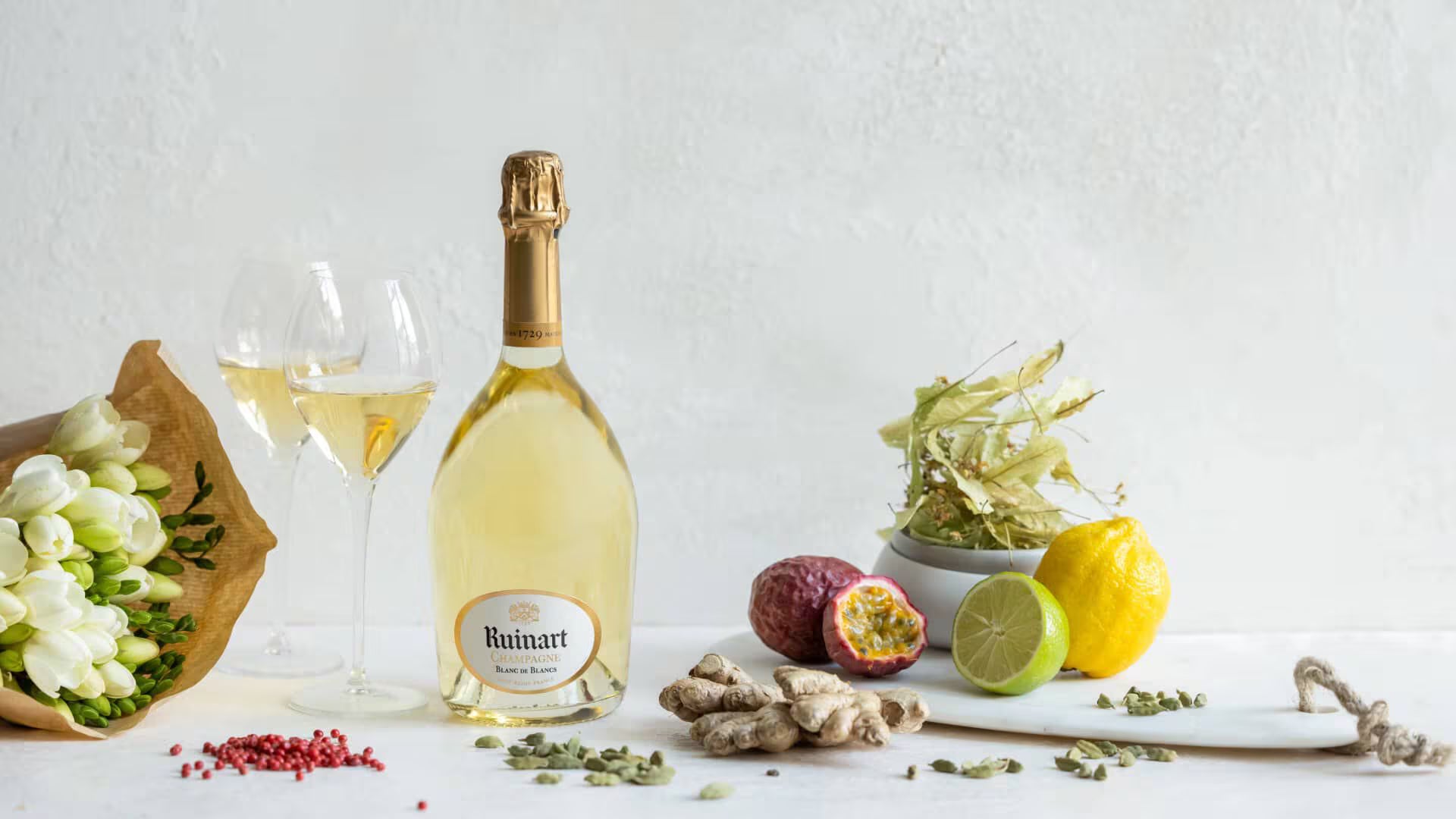 Ruinart Blanc de Blancs champagneflaske, glas og ingredienser som ingefær, lime, og passionfrugt