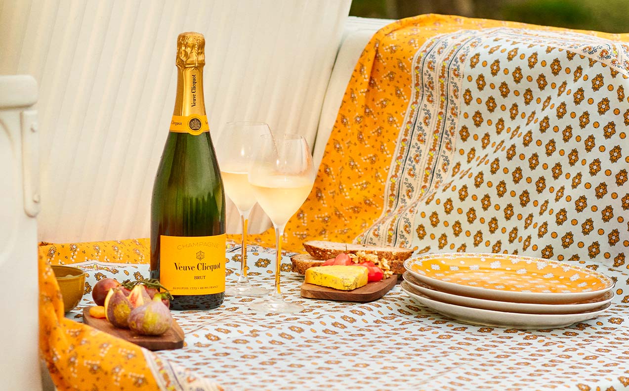 Den ikoniske Gule Enke Champagne på et picnic tæppe med glas og tallerkner