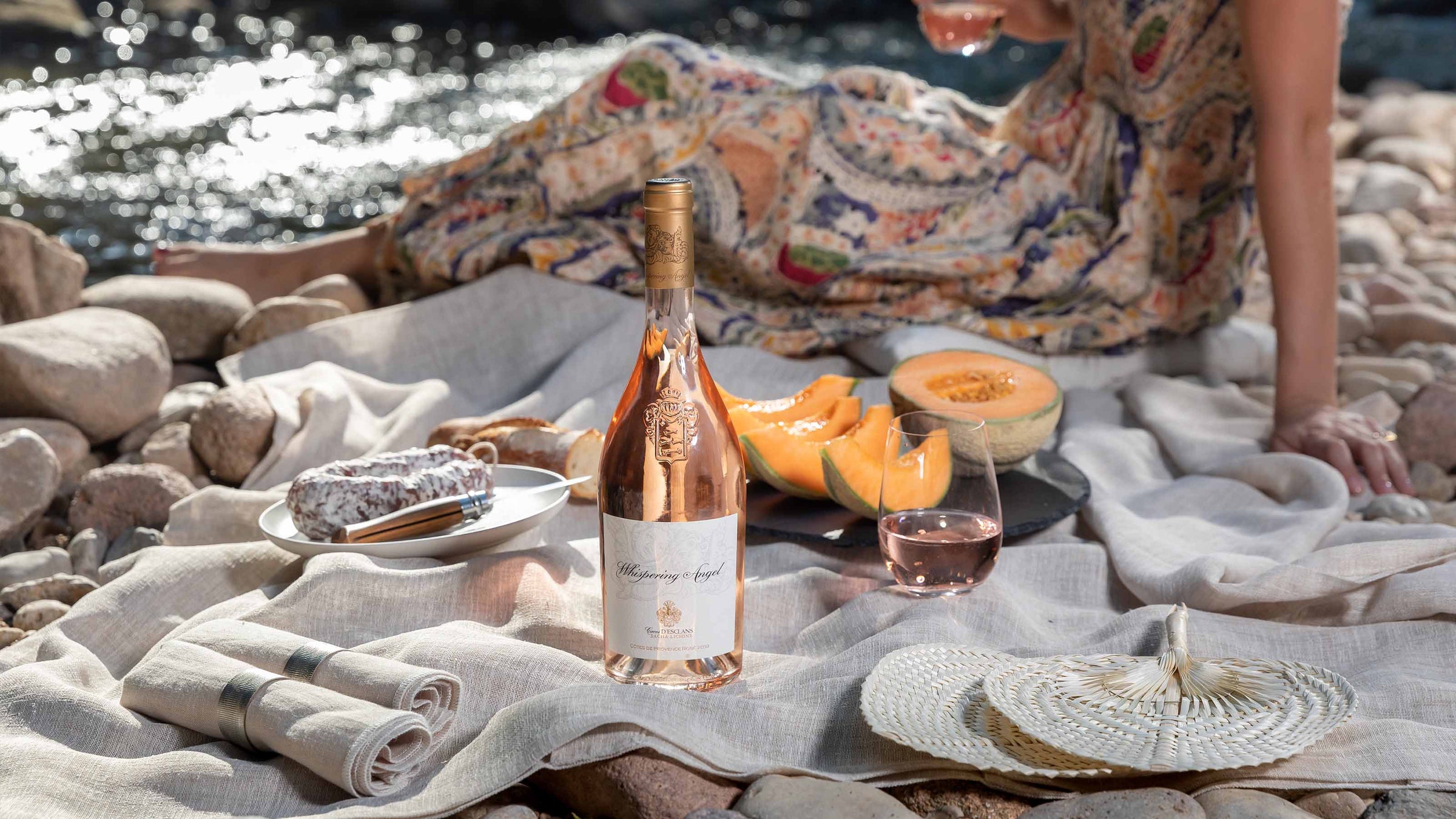 En flaske Whispering Angel rosé på et picknick tæppe med honningsmelon