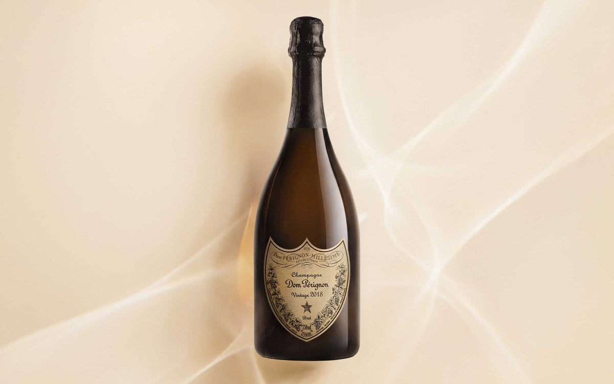 En flaske Dom Pérignon 2018 liggende på en baggrundsfolie, som ligner et sand hav.