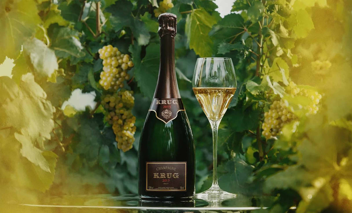 En flaske Krug Vintage 2013 hældt op i glas i en vinmark.