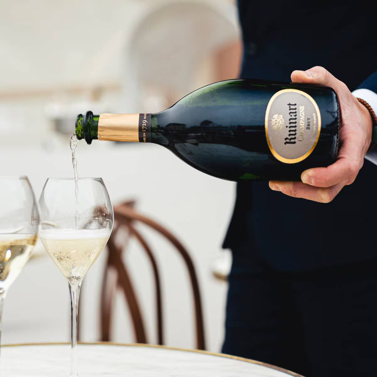 Hænder hælder Ruinart champagne i glas på hvidt bord, elegant scene