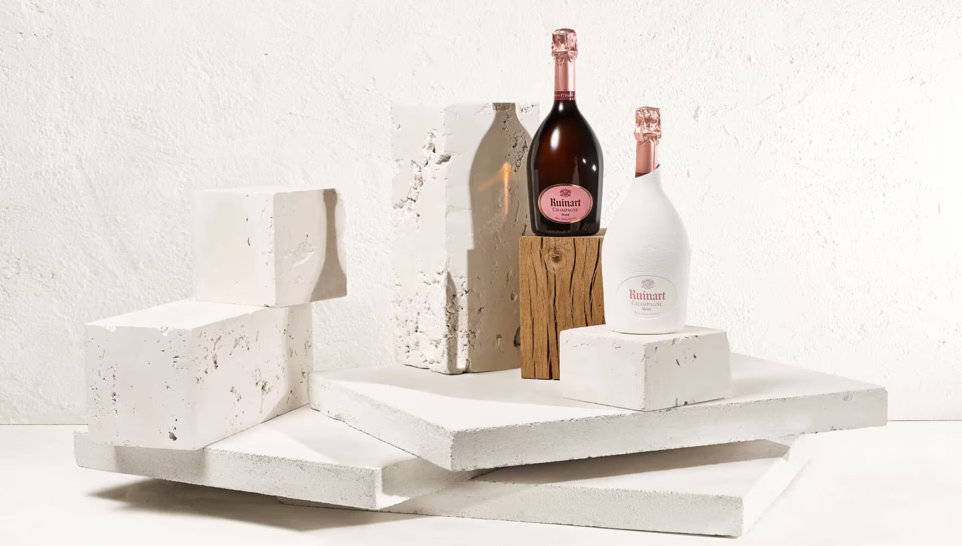 To flasker Ruinart Rosé Champagne på hvide blokke med træ på hvid baggrund