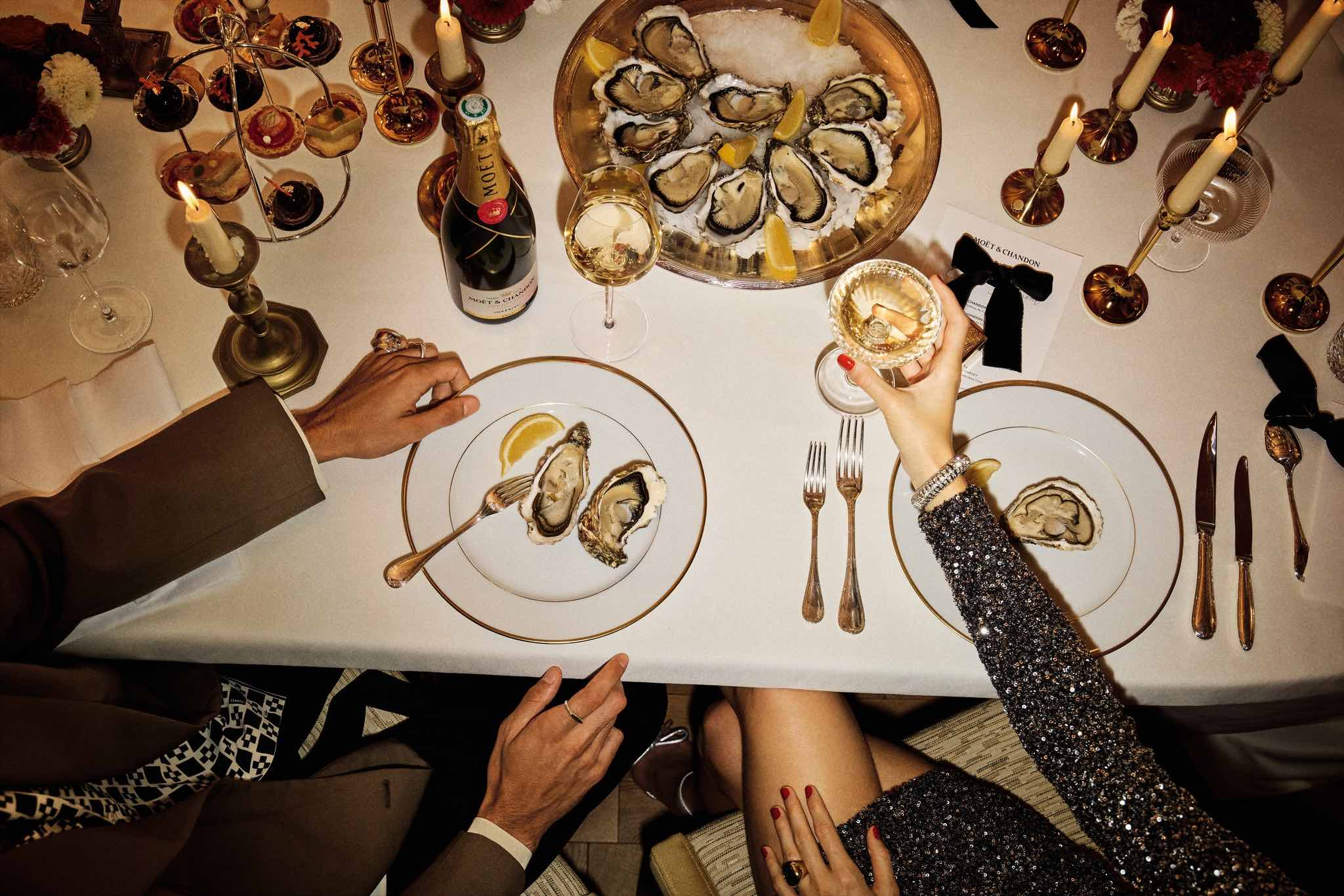 Manden og kvinden spiser østers og drikker champagne ved festligt dækket bord.