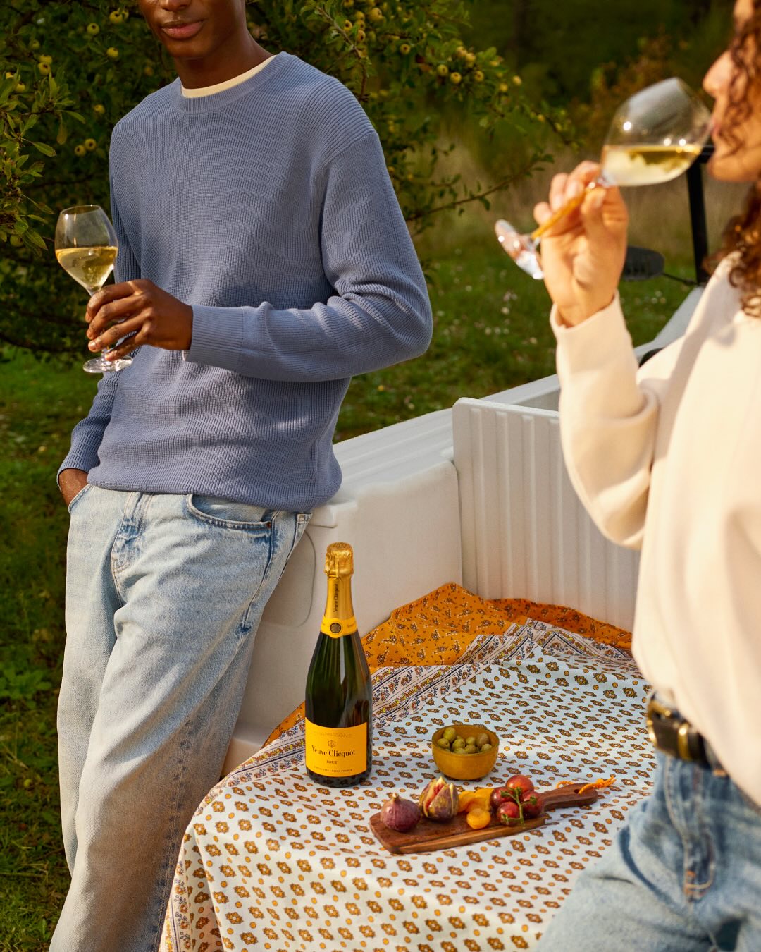 Veuve Clicquot champagneflaske med snacks og drikkende par udendørs på picnictæppe