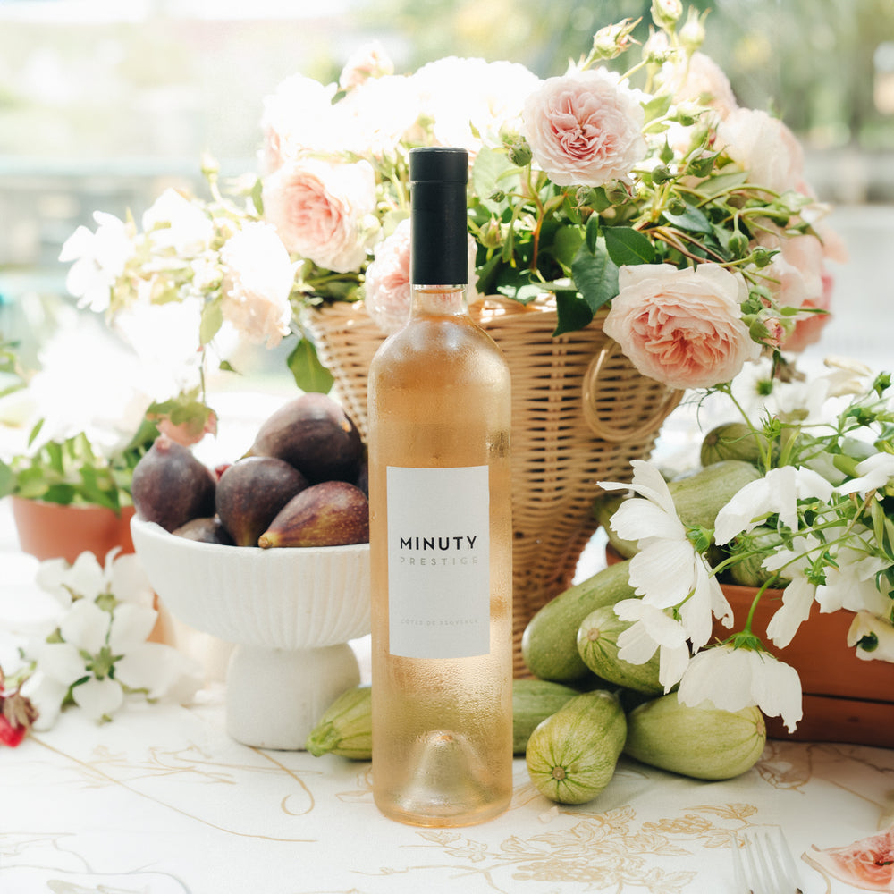 Minuty Prestige rosévin i flaske omgivet af tørrede figner, blomster og grøntsager