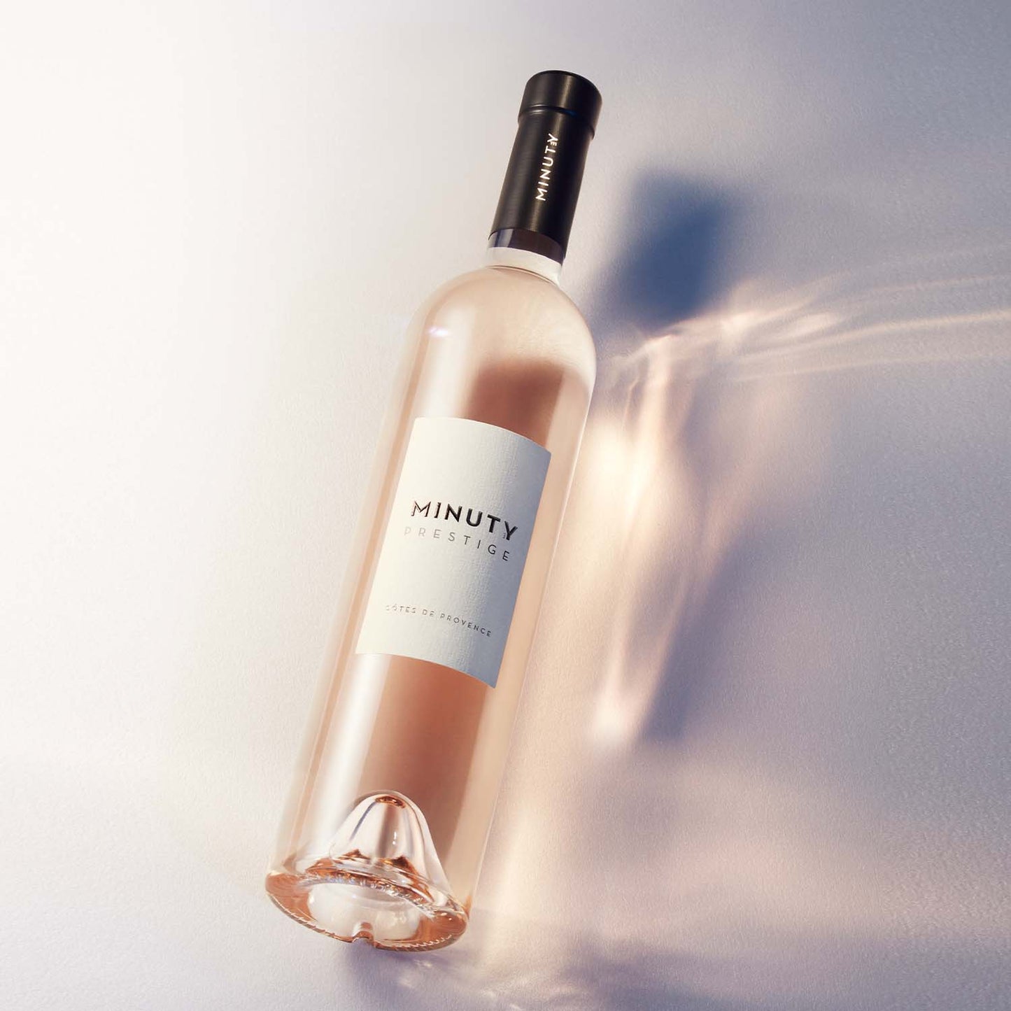 Château Minuty Prestige rosévinflaske liggende på en lys overflade med reflekser