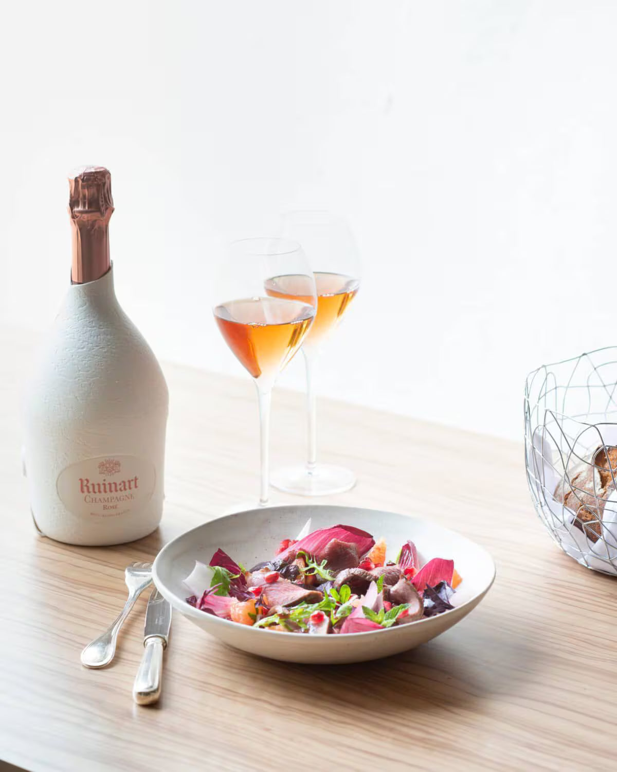 Ruinart Rosé champagneflaske, med salat og to fyldte glas vin