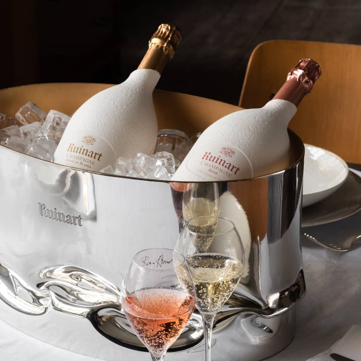 To flasker Ruinart champagne i isspand med to glas fyldt med champagne