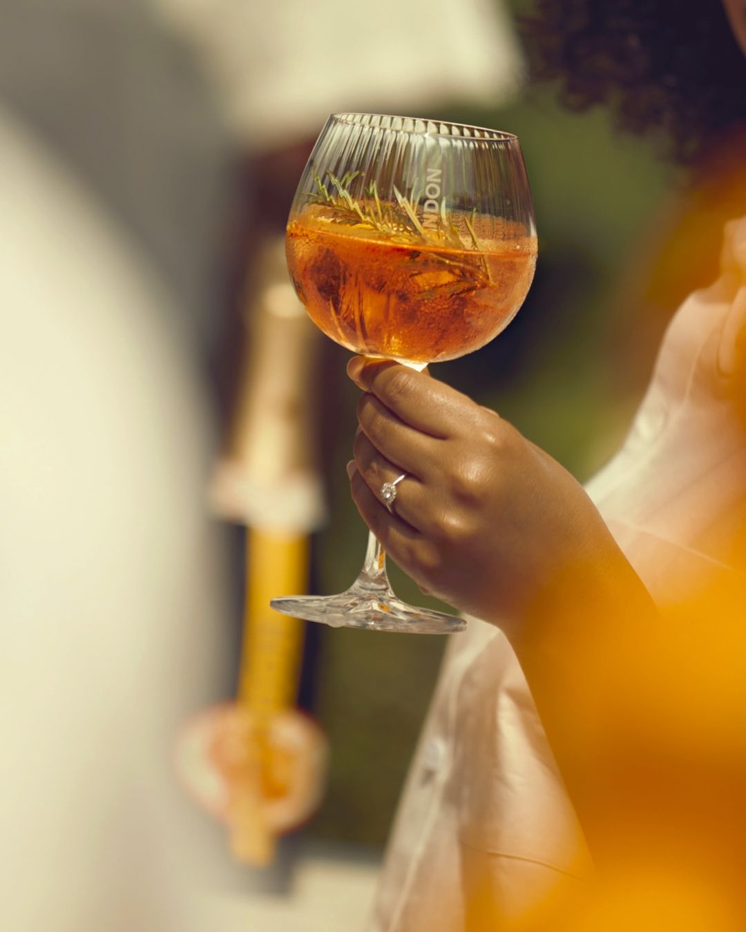 En hånd holder et glas Garden Spritz med rosmarin og is