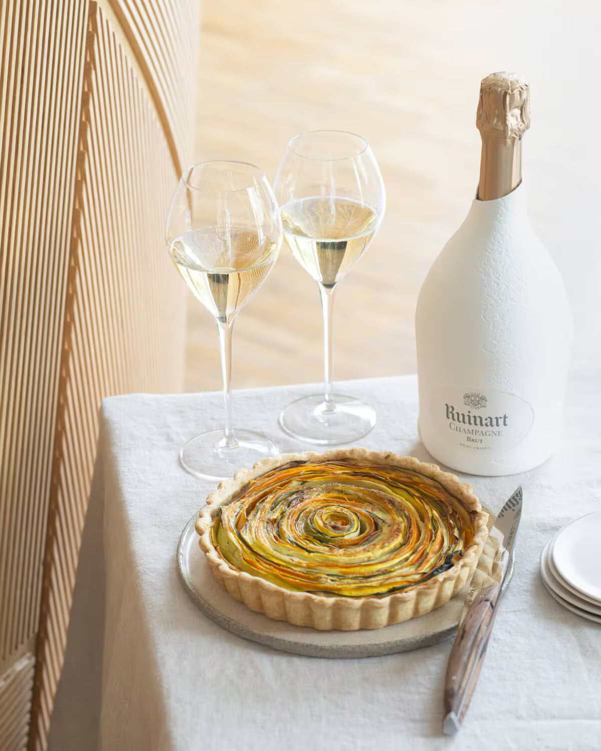 Ruinart champagneflaske, to glas og grøntsagstærte på et hvidt bord
