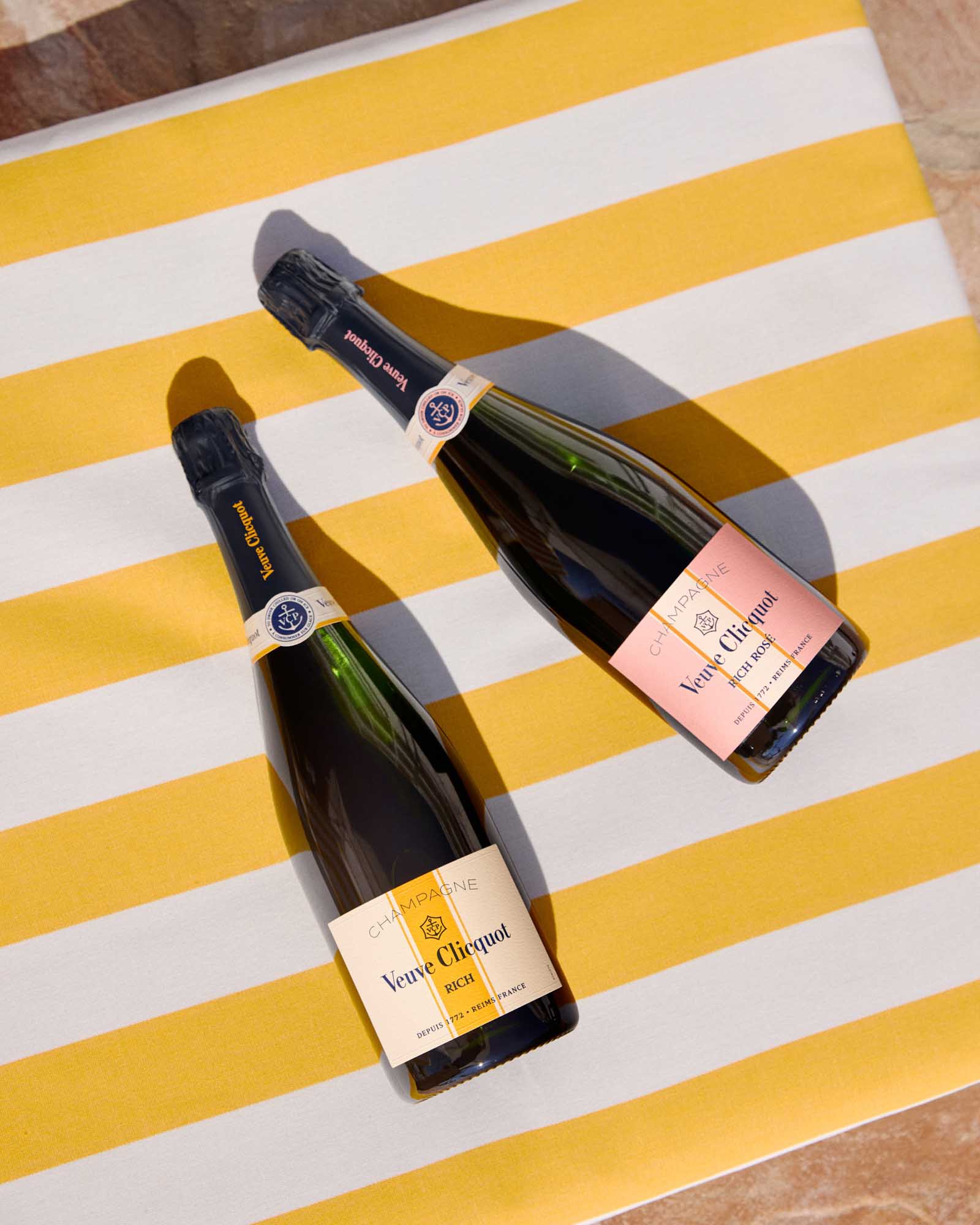 To Veuve Clicquot Rich champagneflasker på et gult og hvidt stribet håndklæde.