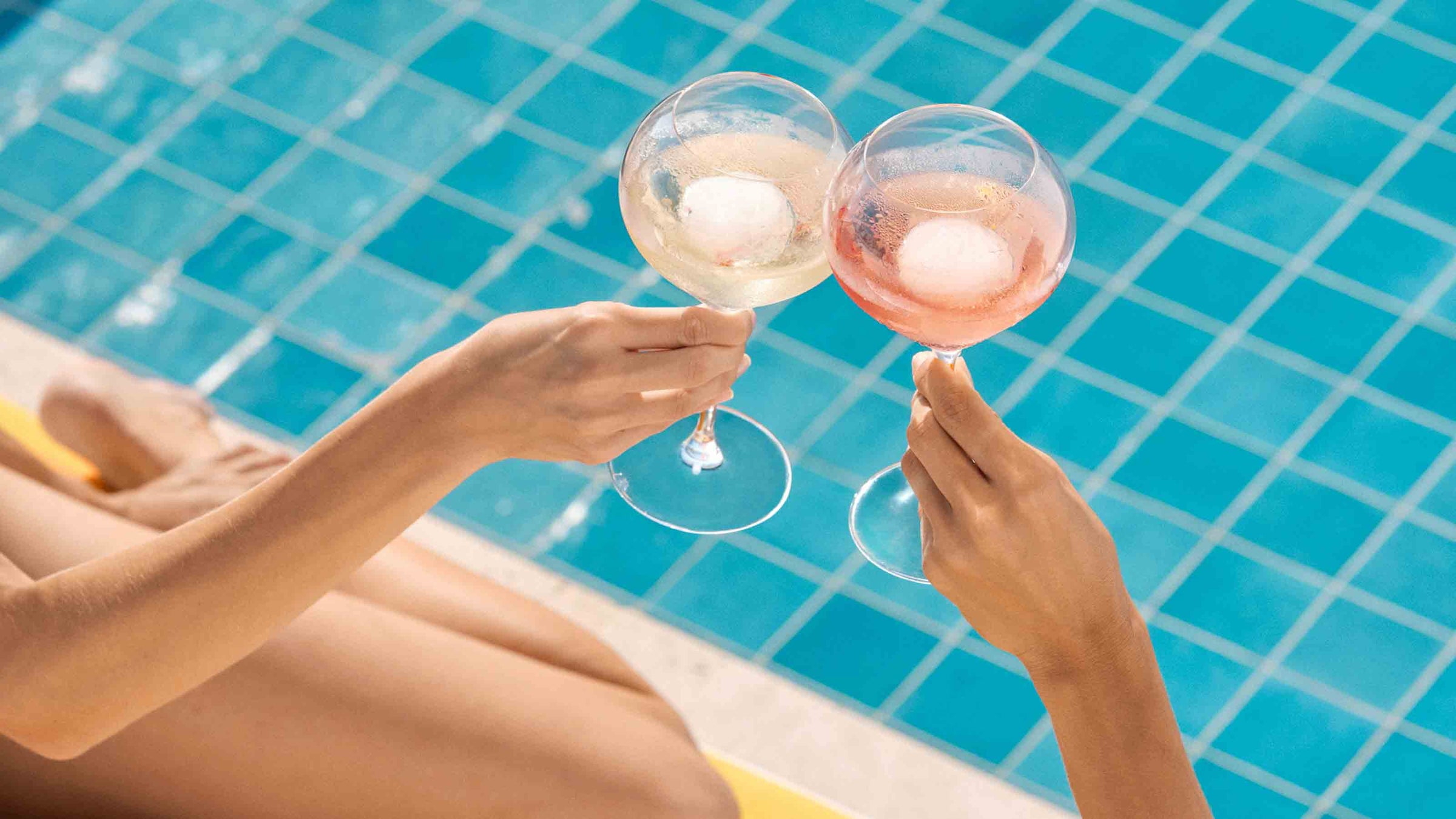 To personer holder champagneglas med isterninger ved en swimmingpool