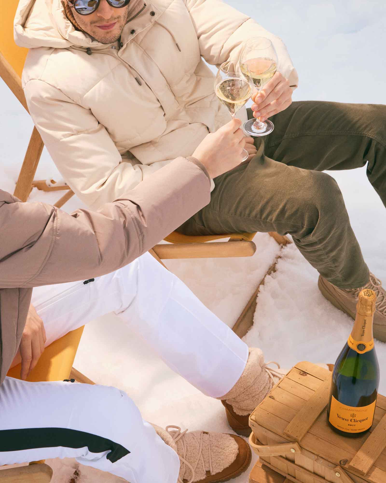 To personer skåler med champagneglas i sneen ved en Veuve Clicquot flaske