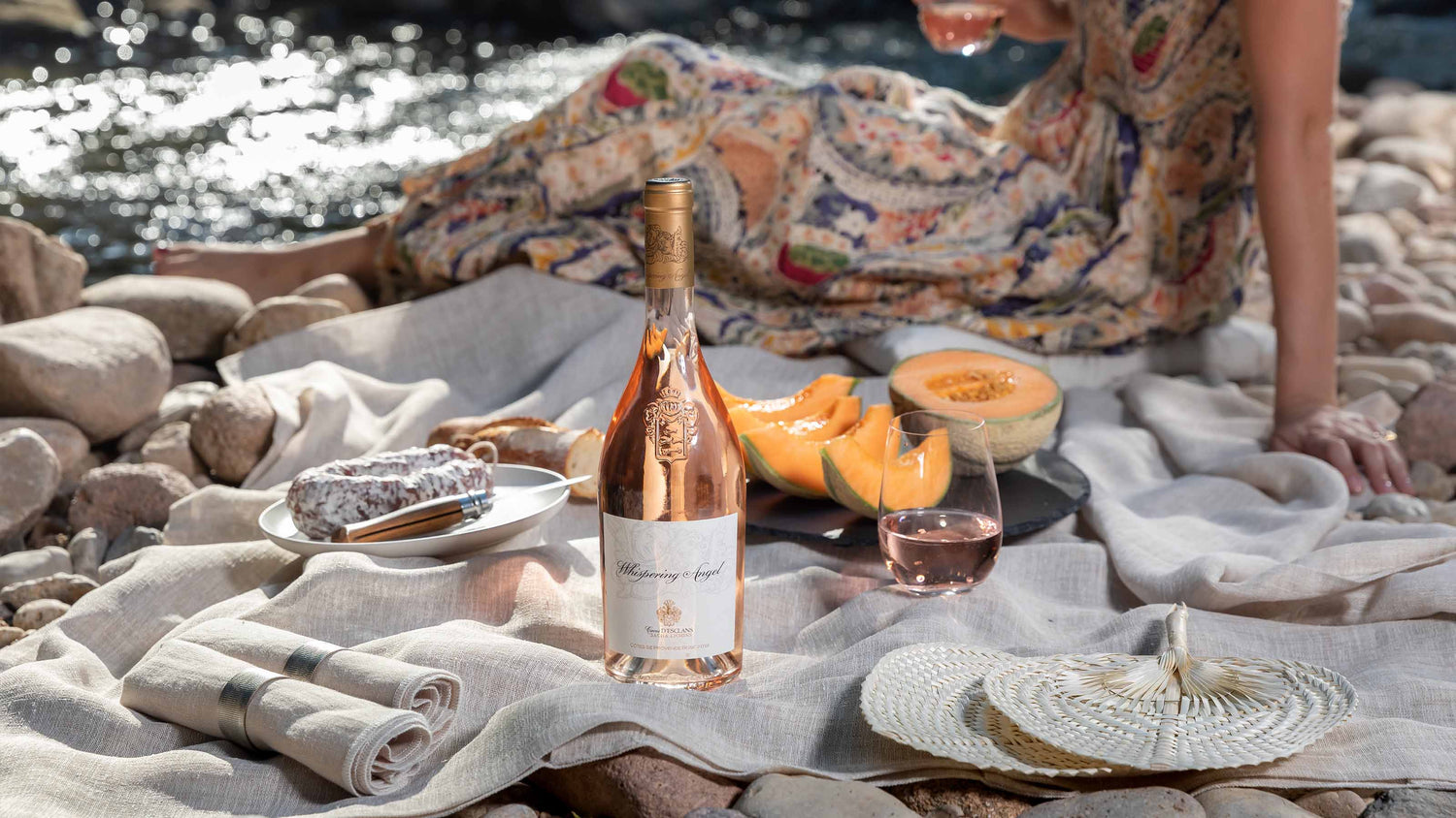 En flaske Whispering Angel rosé på et picknick tæppe med honningsmelon