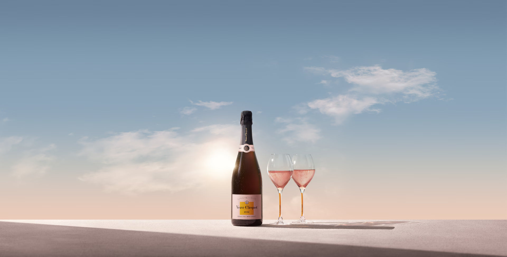 Veuve Clicquot Rosé flaske og to fyldte champagneglas under åben himmel