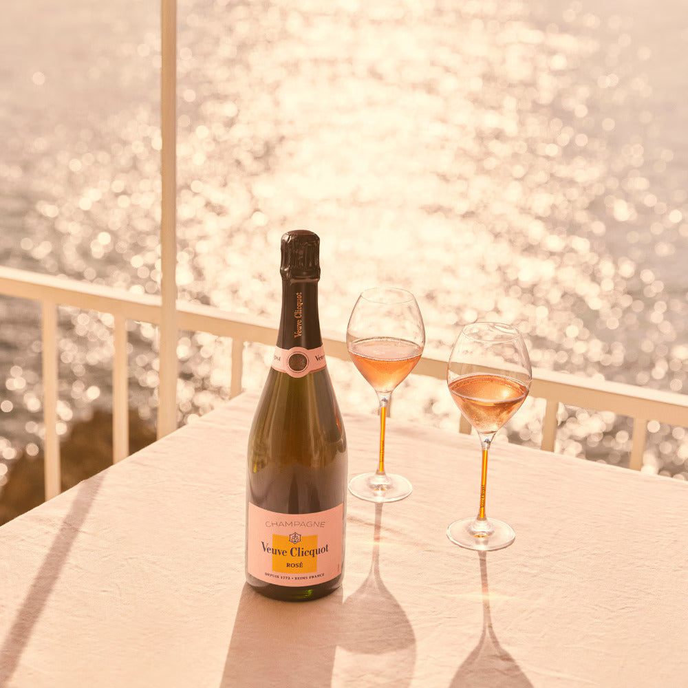 Veuve Clicquot Rosé flaske og to fyldte glas champagne på en terrasse ved vandet